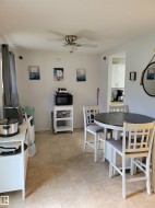 Expansive room featuring light-toned tile flooring, a ceiling fan with integrated lighting, and a partial view into a separate kitchen area with white cabinetry - 