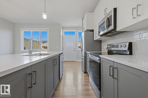 Modern kitchen featuring light wood-finish flooring, two-tone cabinetry with gray lower cabinets and white upper cabinets, white countertops, and a subway tile backsplash - 1364 Keswick Drive Sw, Edmonton, AB 