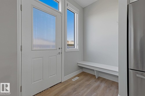 Entryway featuring a panel door with a privacy glass insert, a transom window, wood-finish flooring, a built-in bench, and a stainless steel appliance - 1364 Keswick Drive Sw, Edmonton, AB 