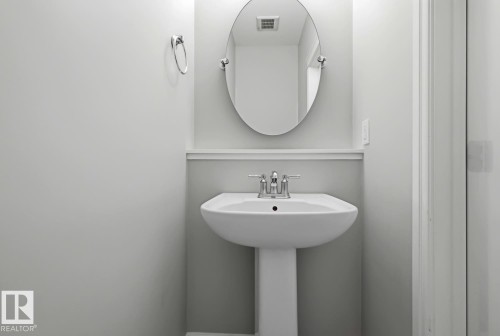 Pedestal sink with chrome-finish faucet and wall-mounted oval mirror - 1364 Keswick Drive Sw, Edmonton, AB 