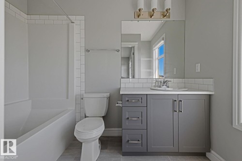 Bathroom featuring a white subway tile surround, a built-in tub with shower, a vanity with gray shaker cabinetry, and a single basin sink - 1364 Keswick Drive Sw, Edmonton, AB 