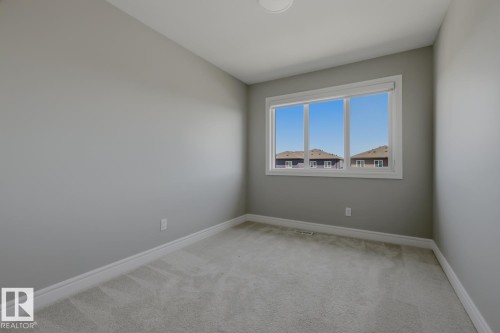 Neutral-toned room featuring a large window, light gray carpeting, and crisp white baseboards - 1364 Keswick Drive Sw, Edmonton, AB 