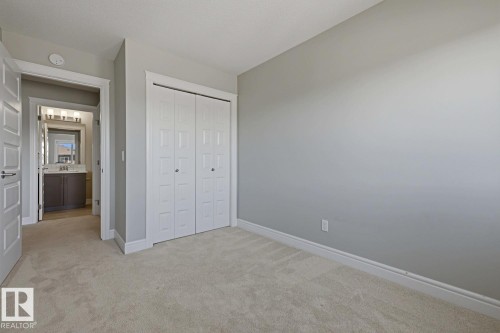 Neutral tone bedroom featuring plush carpeting, white baseboards, and a bi-fold closet with decorative paneling - 1364 Keswick Drive Sw, Edmonton, AB 