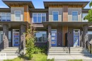 Contemporary townhome exterior featuring stone pillars, a vibrant blue entry door with frosted glass panels, black metal railings, and a multi-textured facade with wood-look and gray paneling accents - 1364 Keswick Drive Sw, Edmonton, AB 