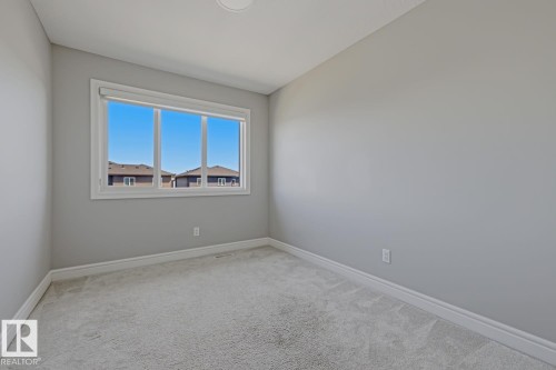 Bright interior room featuring a large window with white trim, light grey walls, and plush grey carpet - 1364 Keswick Drive Sw, Edmonton, AB 