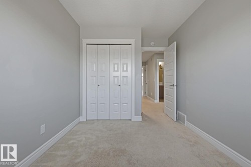 Neutral-toned room featuring a cream carpet, white baseboards, and a bi-fold closet with panel doors - 1364 Keswick Drive Sw, Edmonton, AB 