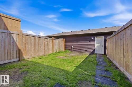 Private backyard area featuring wooden fencing, a grass lawn, a block paver pathway, and a rear exterior door - 1364 Keswick Drive Sw, Edmonton, AB 