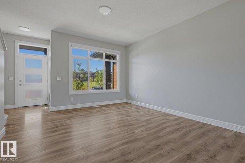 Wood-finish flooring throughout, complemented by a modern front door with frosted glass panels and a transom window - 1364 Keswick Drive Sw, Edmonton, AB 