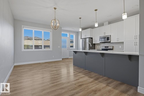 Open-concept kitchen and living area featuring wood-finish flooring, white cabinetry, a gray kitchen island with a white countertop, and stainless steel appliances - 1364 Keswick Drive Sw, Edmonton, AB 