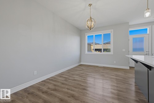 Spacious room featuring wood-finish flooring, a contemporary chandelier, large window, and a door with an upper transom window - 1364 Keswick Drive Sw, Edmonton, AB 