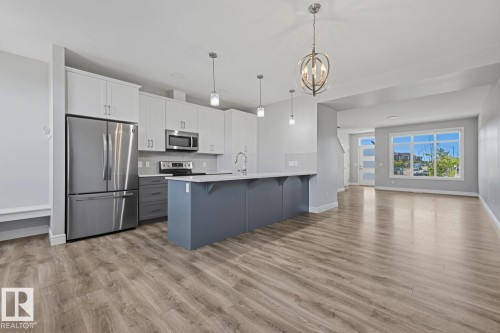 Open-concept kitchen featuring two-tone cabinetry, stainless steel appliances, a center island with a breakfast bar, and wood-finish flooring - 1364 Keswick Drive Sw, Edmonton, AB 