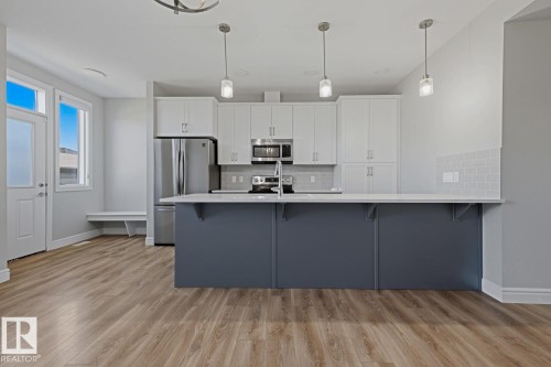 Open-concept kitchen featuring an island with pendant lighting, white shaker cabinetry, stainless steel appliances, and wood-finish flooring - 1364 Keswick Drive Sw, Edmonton, AB 