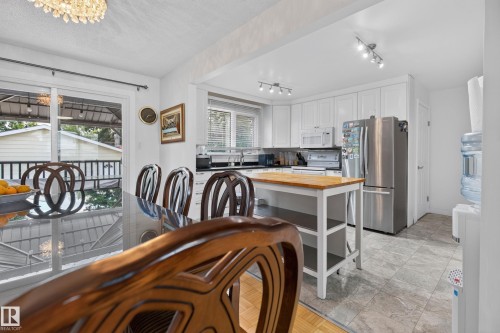 Open-concept kitchen and dining area featuring white cabinetry, stainless steel appliances, and a butcher block island - 18509 92A Avenue, Edmonton, AB 