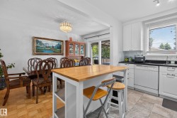 Open-concept kitchen and dining area featuring white cabinetry, a light wood-finish island with seating, dark countertops, and tile flooring - 