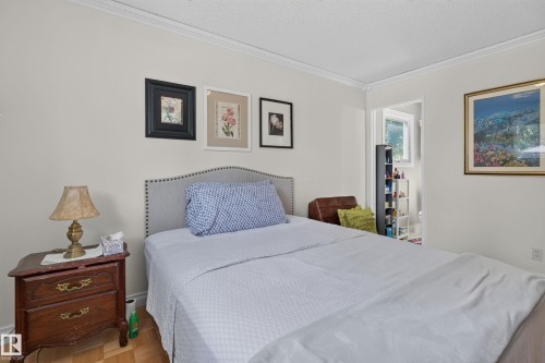 Bedroom featuring a light-colored accent wall, crown molding, and wood-finish flooring - 18509 92A Avenue, Edmonton, AB 