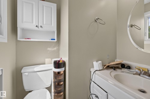 Bathroom featuring a white vanity cabinet with an integrated sink, a circular wall mirror, and a wall-mounted towel ring - 18509 92A Avenue, Edmonton, AB 