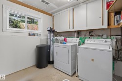 Dedicated laundry area featuring a white sliding window, overhead white cabinetry, and exposed utility piping - 
