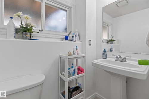 Pedestal sink with chrome faucet, frosted window with white trim, and a wall-mounted mirror - 18509 92A Avenue, Edmonton, AB 