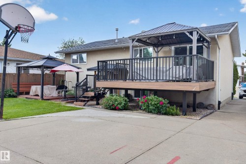 Rear exterior featuring a multi-level deck, a lower patio with a gazebo, a concrete driveway, and a basketball hoop - 18509 92A Avenue, Edmonton, AB 