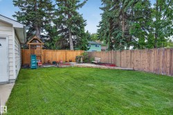 Expansive green lawn surrounded by mature trees, featuring a privacy fence, concrete patio, and a dedicated garden bed - 