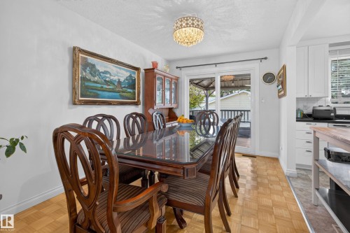 Dining area featuring wood-finish parquet flooring, a decorative overhead light fixture, and a sliding glass door providing access to an exterior deck - 18509 92A Avenue, Edmonton, AB 