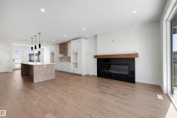 Expansive main level featuring wood-finish flooring, a contemporary fireplace with a black tile surround and wood mantel, a kitchen island with pendant lighting, and abundant natural light from large windows - 