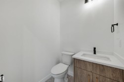 Powder room with a wood-finish vanity, white countertop featuring an integrated sink, and matte black fixtures - 