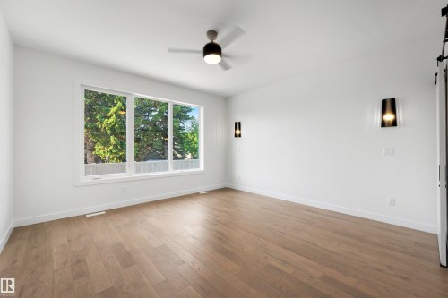 Bright interior space featuring a large three-panel window, wood-finish flooring, a ceiling fan with integrated lighting, and two modern wall sconces - 39 Elsinore Place, Edmonton, AB 