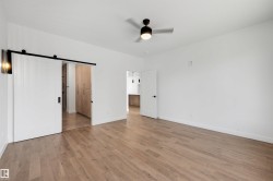 Spacious room with wood-finish flooring and a contemporary ceiling fan - 