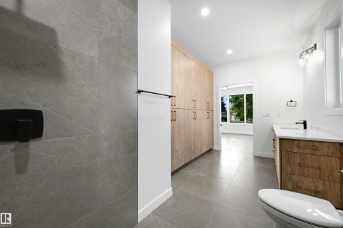 Modern bathroom featuring a floor-to-ceiling custom wood-look storage cabinet, a single vanity with a quartz countertop, and large format grey floor tiles - 39 Elsinore Place, Edmonton, AB 