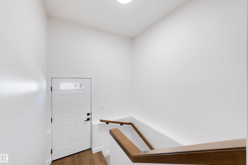 Entryway featuring a white paneled door with lites, wood-finish flooring, and a modern wooden handrail - 39 Elsinore Place, Edmonton, AB 