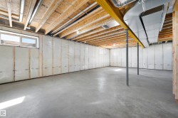 Unfinished lower level featuring concrete flooring, exposed wood joists, a steel support beam, two windows, and insulated walls - 