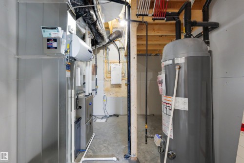 Utility room featuring a water heater, furnace, and exposed ceiling joists with various piping - 39 Elsinore Place, Edmonton, AB 