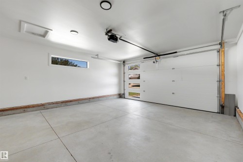 Spacious garage featuring a concrete floor, white walls, modern overhead lighting, and an automatic garage door with rectangular window inserts - 39 Elsinore Place, Edmonton, AB 