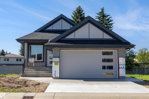 Modern exterior with a light gray garage door featuring frosted glass panels, dark gray siding, a dark shingle roof, and an inviting concrete driveway - 39 Elsinore Place, Edmonton, AB 