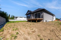 Newly constructed home featuring grey siding, a dark shingle roof, and a rear deck with black railings - 