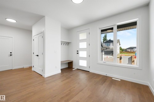 Entryway featuring wood-finish flooring, a modern front door with frosted glass panels, a built-in bench with coat hooks, crisp white walls, and a large window providing ambient light - 39 Elsinore Place, Edmonton, AB 