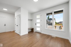 Entryway featuring wood-finish flooring, a modern front door with frosted glass panels, a built-in bench with coat hooks, crisp white walls, and a large window providing ambient light - 