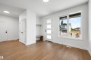 Entryway featuring wood-finish flooring, a modern front door with frosted glass panels, a built-in bench with coat hooks, crisp white walls, and a large window providing ambient light - 39 Elsinore Place, Edmonton, AB 