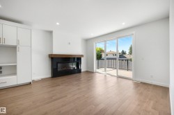 Living area featuring wood-finish flooring, a modern black fireplace with a wood mantle, built-in white cabinetry with gold hardware, recessed lighting, and a sliding glass door opening to an outdoor balcony - 