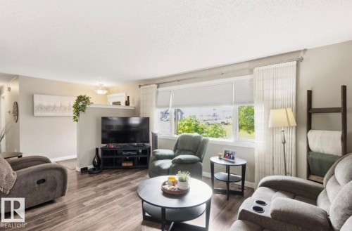 Living area featuring wood-finish flooring, a large window with roller shades, and light neutral wall colors - 4007 45 Street, Stony Plain, AB 