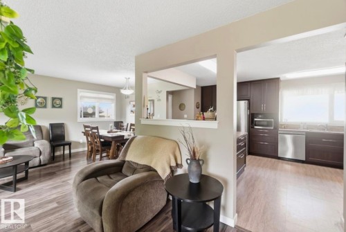 Open concept living area with wood-finish flooring, a dining space, and a kitchen featuring dark cabinetry, stainless steel appliances, and a pass-through window - 4007 45 Street, Stony Plain, AB 