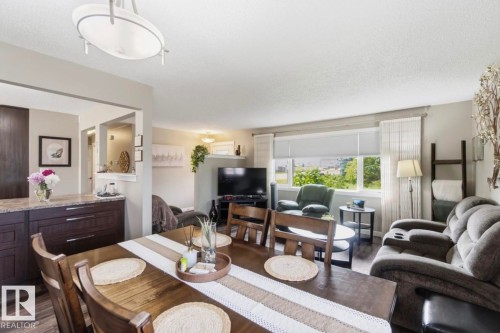 Open-concept living and dining areas featuring wood-finish flooring, a large picture window, and a built-in kitchen peninsula with a stone countertop and dark wood cabinetry - 4007 45 Street, Stony Plain, AB 