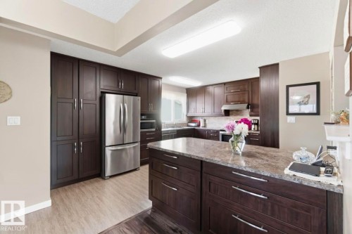 Kitchen featuring dark wood-finish cabinetry, stainless steel appliances, and a large central island with a stone-finish countertop - 4007 45 Street, Stony Plain, AB 