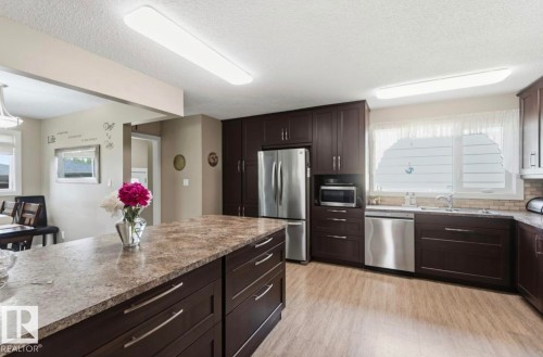 Kitchen featuring a spacious island with stone-look countertop, dark wood-finish cabinetry, stainless steel appliances, and wood-finish flooring - 4007 45 Street, Stony Plain, AB 
