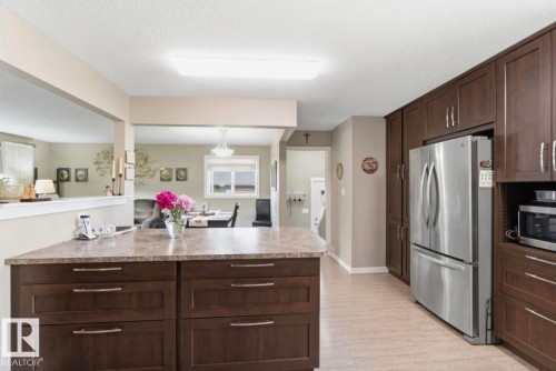 Kitchen featuring abundant dark wood cabinetry, a stainless steel refrigerator, and a built-in microwave - 4007 45 Street, Stony Plain, AB 