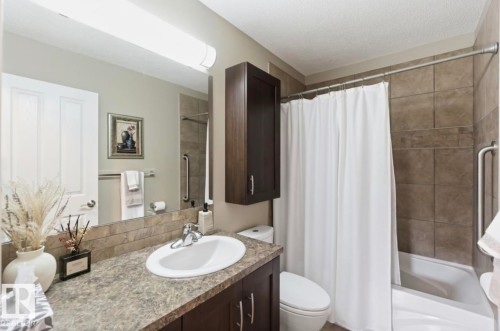 Bathroom featuring a white porcelain sink, dark wood-finish cabinetry, speckled countertop, and a tiled shower/tub combination with grab bars - 4007 45 Street, Stony Plain, AB 