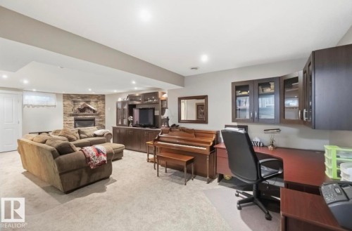Spacious finished lower level featuring a stone-faced fireplace, recessed lighting, built-in media cabinetry, and a dedicated desk area with upper cabinets - 4007 45 Street, Stony Plain, AB 