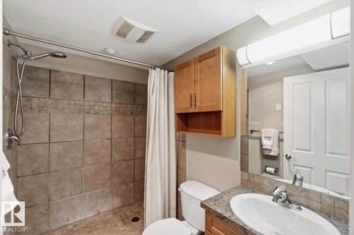 Full bathroom featuring a tiled shower with a handheld showerhead, a single vanity with a laminate countertop, a wood-finish wall cabinet, and an overhead mirror with strip lighting - 4007 45 Street, Stony Plain, AB 