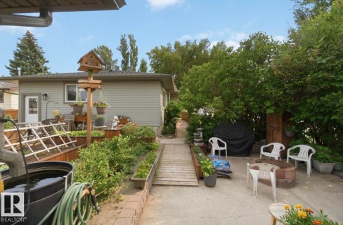 Expansive backyard featuring a concrete patio, built-in fire pit, terraced garden beds, wood walkway, and mature perimeter trees - 4007 45 Street, Stony Plain, AB 